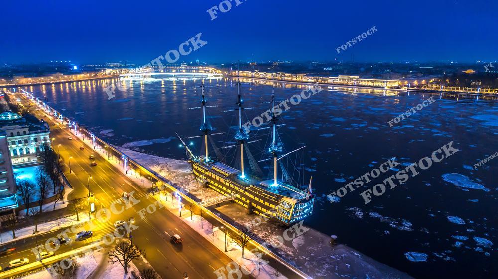 Панорамная фотография реки Невы в Санкт-Петербурге зимой, снятая с высоты птичьего полета. На снимке видны льдины, медленно плывущие по реке, замерзшие участки воды и архитектура набережных города. Съемка с дрона позволяет оценить масштаб реки, зимний городской пейзаж и красоту северной столицы России в холодное время года. Фотография передает атмосферу зимнего Петербурга, морозный пейзаж и спокойствие водной глади, идеально подходя для туристических публикаций, фотостоков, оформления интерьеров, рекламы и материалов о зимнем Петербурге.